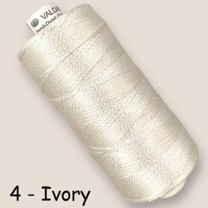 May include: A spool of ivory colored thread wound in a cylindrical shape. The top of the spool features a white label with the text VALDANI Hand-Dyed. The bottom left corner of the image displays the black text 4 - Ivory, identifying the color.