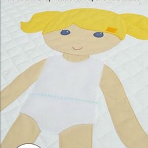 May include: A white quilted blanket featuring a large applique of a doll with yellow hair in pigtails, blue eyes, and a white top. The text reads Paper Doll Blanket, Hook and Loop Fabric for Paper Doll Blanket, and Contains materials for quilt.