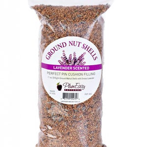 May include: A clear plastic bag filled with ground walnut shells, lavender-scented, for pin cushion filling. The bag has a label with text that reads "Ground Nut Shells" and "Lavender Scented". The bag contains 11 oz. (312g) of ground walnut shells.