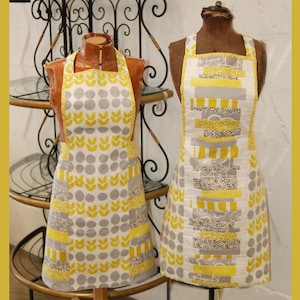 May include: Two aprons displayed on mannequins, featuring yellow and gray geometric patterns. The left apron has a repeating leaf and circle motif, while the right apron displays horizontal fabric strips with floral and polka dot designs.