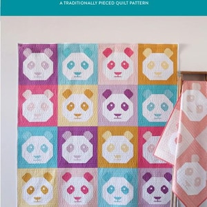 May include: A colorful quilt with panda faces in various colors, including pink, purple, yellow, and blue. The quilt is displayed on a wall, with a matching quilt folded on a wooden ladder. The text "PANDAMONIUM" is at the top.