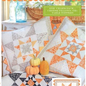 May include: Image features two star-patterned pillows and a table runner with a matching design. The pillows and runner showcase a patchwork design in white, orange, gray, and black. The text "Stars of the Harvest" is at the top.