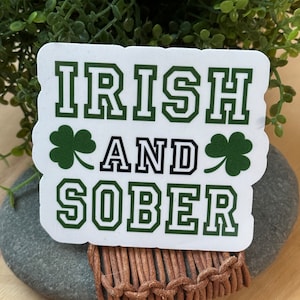 May include: White sticker with green text that reads "IRISH AND SOBER" with a shamrock on either side of the word "AND".
