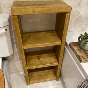 May include: A three-tiered wooden shelf unit with a rustic brown finish. The shelf is made of reclaimed wood and has a natural, distressed look. It is perfect for storing bathroom essentials or displaying decorative items.
