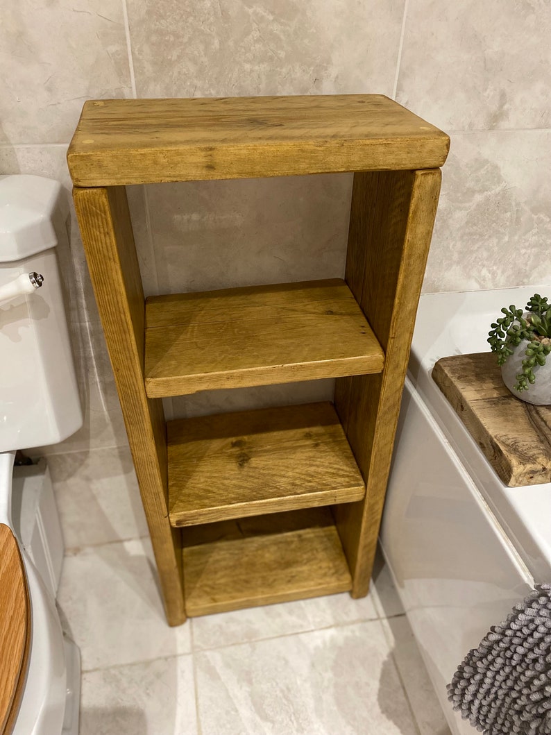 May include: A three-tiered wooden shelf unit with a rustic brown finish. The shelf is made of reclaimed wood and has a natural, distressed look. It is perfect for storing bathroom essentials or displaying decorative items.