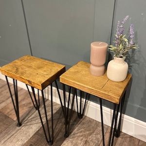 May include: Two rectangular side tables with natural wood grain tops and black metal hairpin legs. One table holds a ribbed mauve pillar candle and a small white ceramic vase containing artificial purple lavender sprigs.