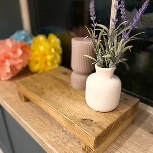 May include: A rectangular wooden riser with a natural grain finish, featuring a small white ceramic vase filled with purple lavender sprigs and a cylindrical mauve ribbed candle placed on its surface, creating a layered display arrangement.
