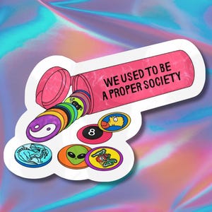 May include: A sticker featuring a pink pill bottle with the text "WE USED TO BE A PROPER SOCIETY." The bottle is spilling out colorful circular designs, including a yin-yang symbol, an eight ball, and a cartoon character.