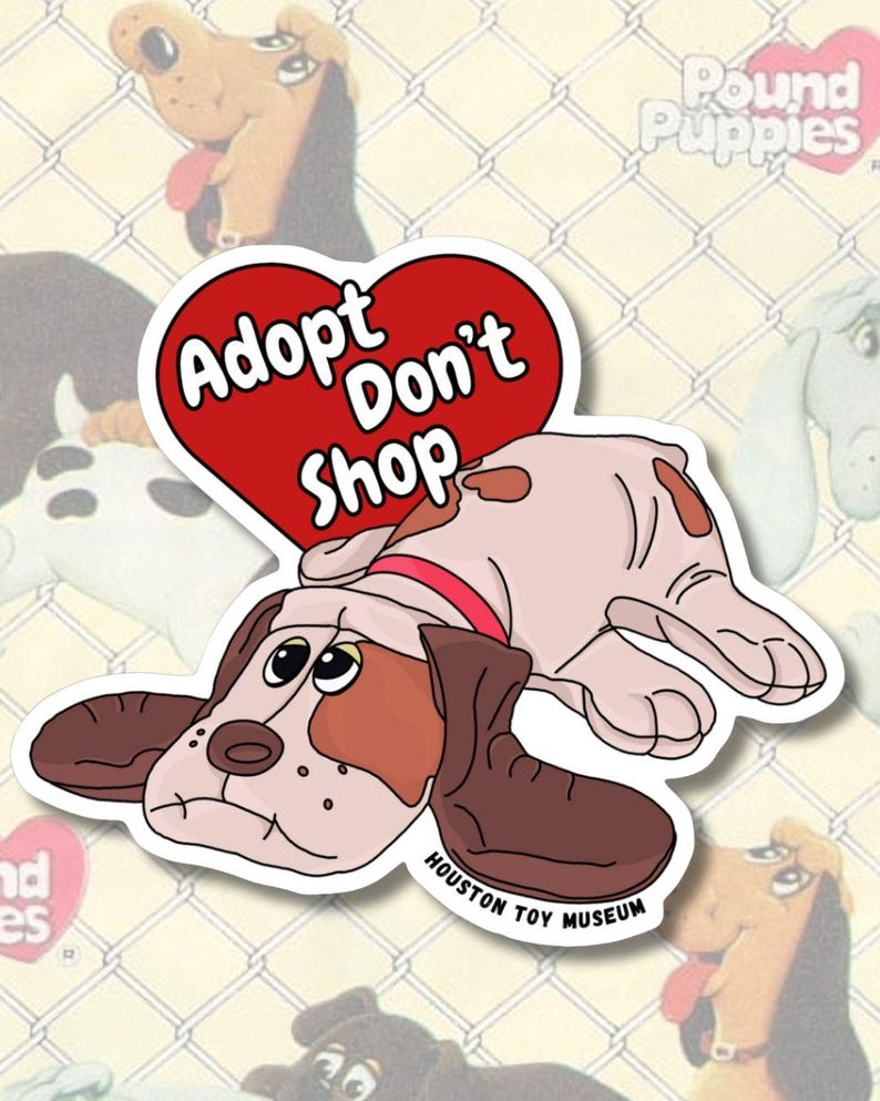 May include: A sticker depicting a cartoon dog with brown and white fur, wearing a red collar, and a red heart with the words "Adopt Don't Shop." The sticker is from the Houston Toy Museum and has a white border.