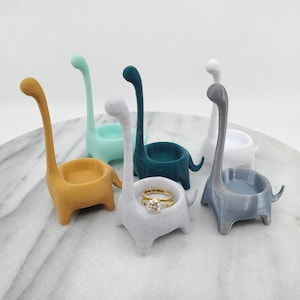 Peut inclure: Six porte-bagues en forme de dinosaure de différentes couleurs. Les porte-bagues sont en plastique lisse et texturé. Un porte-bague contient une bague.