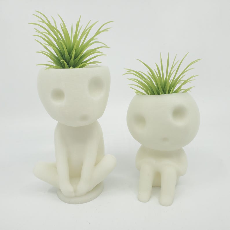 Puede incluir: Dos macetas de cer&aacute;mica blanca con forma de peque&ntilde;as figuras humanas con plantas verdes que crecen de sus cabezas.