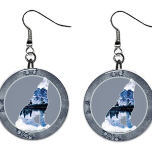 May include: A pair of silver dangle earrings with a round, gray and blue design. The design features a wolf silhouette with a wintery landscape inside. The wolf is howling at the moon.