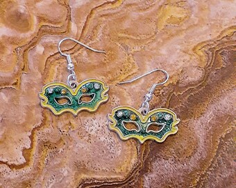 May include: A pair of silver earrings with green and yellow masquerade masks. The masks have rhinestones and are detailed with black lines.