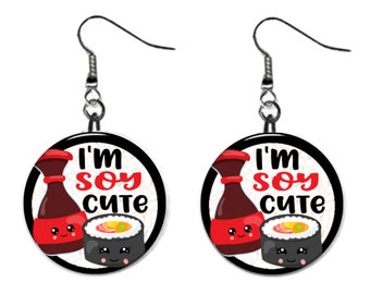 May include: A pair of earrings with a black and white circle design. The circle features a cartoon soy sauce bottle and a sushi roll with the text "I'm soy cute".