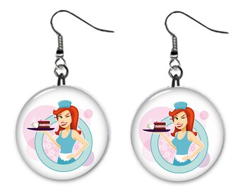 May include: A pair of silver dangle earrings with a round, white, and blue design. The design features a cartoon woman with red hair wearing a blue and white uniform holding a tray with a slice of cake and a cup of coffee. The background is pink with white flowers.