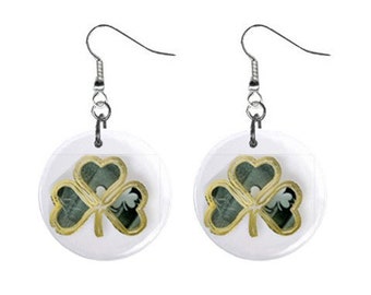 May include: A pair of silver dangle earrings with a white circular charm featuring a gold shamrock design.