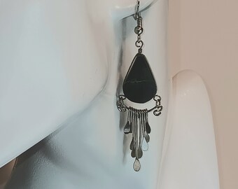 May include: Silver dangle earrings with a black teardrop-shaped stone and a fringe of silver beads.
