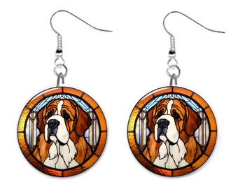 May include: A pair of silver dangle earrings with a round stained glass design featuring a Saint Bernard dog. The dog is brown and white with a black nose and is framed in a gold and orange stained glass design.
