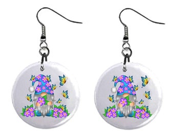 May include: A pair of dangle earrings featuring a gnome with a purple and blue flower hat and a white beard. The gnome is holding a purple flower and is surrounded by butterflies and purple flowers. The earrings are on a white background.