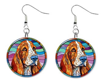 May include: A pair of silver dangle earrings with a round, colorful stained glass design featuring a basset hound dog. The dog's face is in the center of the circle, with a rainbow-colored background.