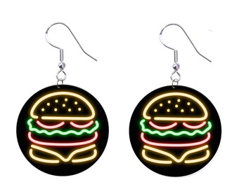 May include: A pair of round earrings featuring a neon-style burger design. The burger is outlined in yellow, red, and green against a black background. The earrings have silver-colored fish hook ear wires.