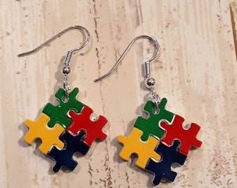May include: A pair of silver dangle earrings with puzzle piece charms. The puzzle pieces are made of four different colors: red, yellow, green, and blue.