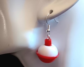 May include: Red and white fishing bobber dangle earrings. The bobber is made of plastic and has a silver hook.
