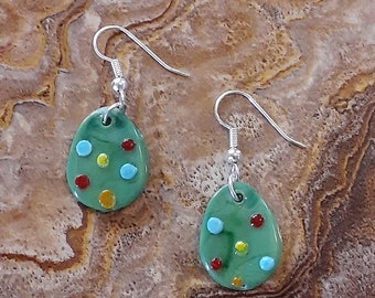 May include: A pair of green oval-shaped earrings with silver hooks. The earrings are decorated with red, yellow, and blue dots.