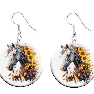 May include: A pair of earrings featuring a white and brown spotted horse with a mane of sunflowers. The earrings are round and have a silver hook.