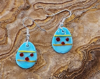 May include: A pair of blue egg-shaped earrings with red and yellow accents. The earrings are made of glass and have a silver hook.