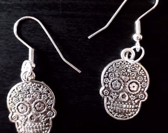 May include: A pair of silver dangle earrings featuring a detailed sugar skull design with floral accents.