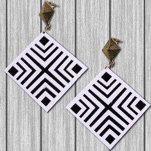 May include: A pair of black and white geometric earrings with gold accents. The earrings are square shaped with a black and white geometric pattern.