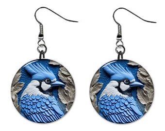 May include: A pair of blue jay earrings with a detailed, 3D-like design. The earrings are round and feature a blue jay with white and black markings against a blue and gray background.