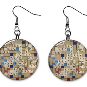 May include: A pair of round, silver earrings with a Scrabble board design. The board features a variety of letters and numbers in blue, red, and white.