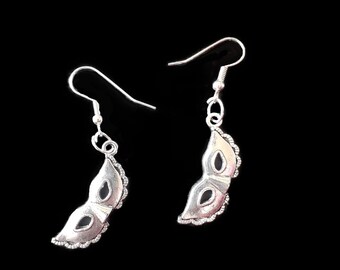 May include: A pair of silver earrings with a masquerade mask design. The masks are detailed with a scalloped edge and have a black center.