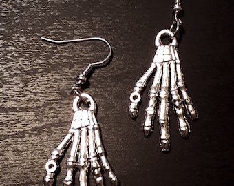 May include: A pair of silver skeleton hand earrings. The earrings are dangling and feature a detailed skeleton hand design.