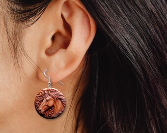 May include: A pair of silver dangle earrings with a round brown wooden charm featuring a carved horse head design.