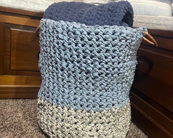 May include: A blue and white crocheted storage basket with a wooden handle. The basket is sitting on a brown carpet.