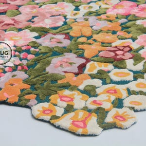 Pu&ograve; includere: Un tappeto floreale con sfondo turchese e un motivo di fiori colorati nelle tonalit&agrave; del rosa, arancione e bianco. Il tappeto ha un bordo ritagliato e un logo di "The Rug Company".