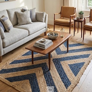 Op de afbeelding: Een witte keramische mok met een zwart oor en de tekst "But First, Coffee" in een vetgedrukte, zwarte letter. De mok is gevuld met een donkere vloeistof, waarschijnlijk koffie, en staat op een lichtgekleurd oppervlak.