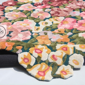 Pu&ograve; includere: Un tappeto floreale con sfondo verde acqua scuro e un motivo di fiori rosa, pesca e bianchi. Il tappeto ha una trama a pelo tagliato e un retro grigio scuro. Il logo The Rug Company &egrave; visibile.