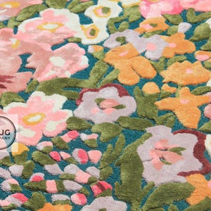 Pu&ograve; includere: Primo piano di un tappeto floreale con sfondo turchese. Il tappeto presenta un motivo di fiori rosa, arancioni e bianchi con foglie verdi. I fiori hanno un aspetto strutturato e in rilievo.