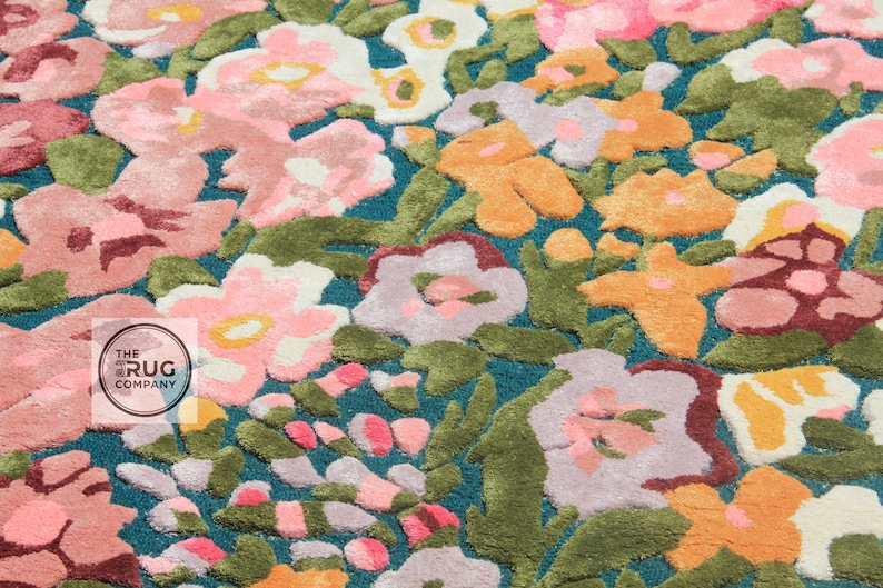 Pu&ograve; includere: Primo piano di un tappeto floreale con sfondo turchese. Il tappeto presenta un motivo di fiori rosa, arancioni e bianchi con foglie verdi. I fiori hanno un aspetto strutturato e in rilievo.