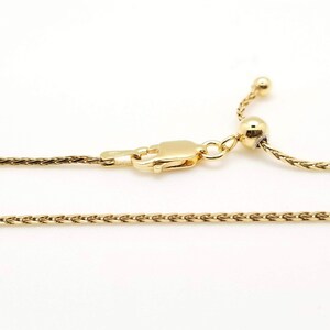 Puede incluir: Un collar dorado con un dise&ntilde;o de cadena de trigo. El collar presenta un cierre de mosquet&oacute;n y una cuenta ajustable en el extremo. La joya est&aacute; sobre un fondo blanco.