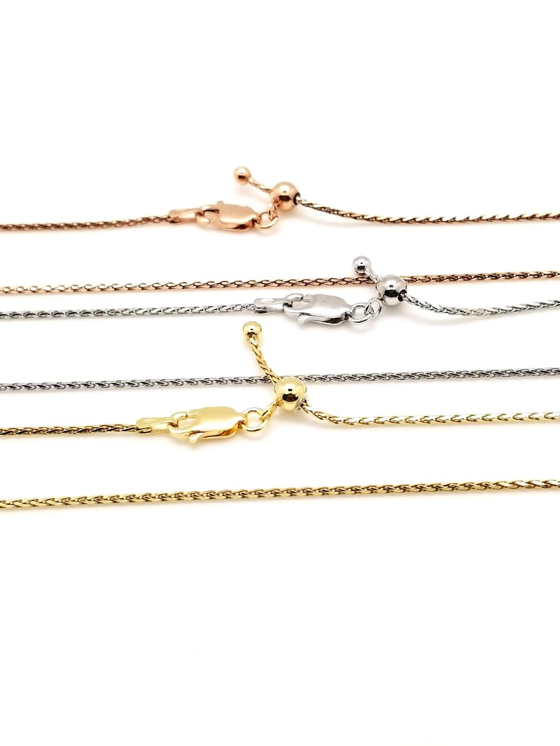 Puede incluir: Primer plano de cuatro collares ajustables de cadena de trigo en tonos oro rosa, plata y oro. Cada collar presenta un cierre de mosquet&oacute;n y una cuenta deslizante para ajustar la longitud. Las cadenas se muestran sobre un fondo blanco.