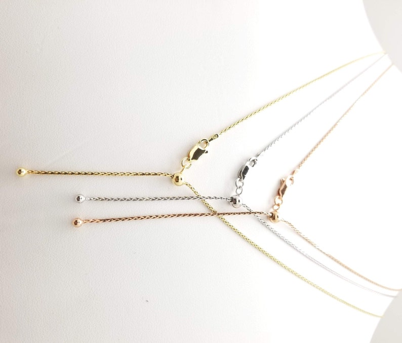 Puede incluir: Cuatro collares de cadena ajustables en tonos oro, plata y oro rosa. Cada collar presenta una delicada cadena con una cuenta deslizante para ajustar la longitud y un cierre de mosquet&oacute;n. Se muestran sobre un fondo blanco.