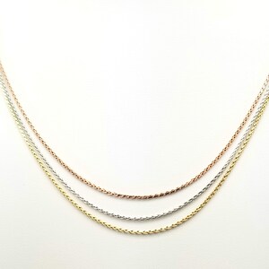 Puede incluir: Tres delicados collares en tonos oro, plata y oro rosa. Las cadenas tienen un dise&ntilde;o de trigo, cada una paralela a las otras sobre un fondo blanco. Los collares probablemente est&aacute;n hechos de metales preciosos.