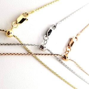 Puede incluir: Primer plano de varios collares delicados en oro, plata y oro rosa. Cada collar presenta una fina cadena con un cierre de mosquet&oacute;n y una cuenta ajustable. Las cadenas se muestran sobre un fondo blanco.