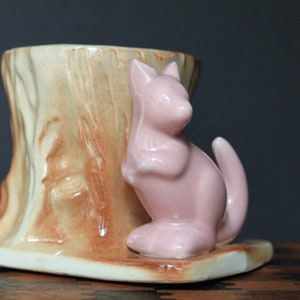 May include: A ceramic planter shaped like a tree stump with a pink kangaroo figurine attached to the side.