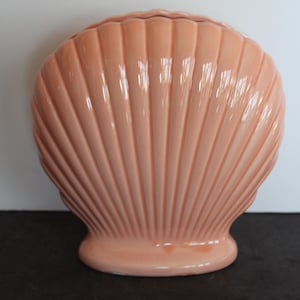 May include: A peach-colored ceramic seashell vase. The vase is shaped like a large seashell with a smooth, glossy finish.